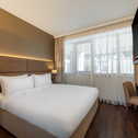 Modernes Hotelzimmer mit Doppelbett, TV, Schreibtisch und großen Fenstern | © Name