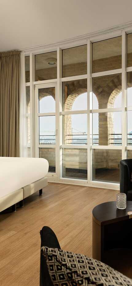A modern bedroom features a large bed and a stunning view through arched windows, with elegant decor enhancing the ambiance.