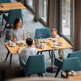 A woman and two children enjoy breakfast together at a modern restaurant, with sunlight streaming through large windows.