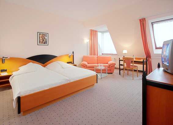 Ein gemütliches Doppelzimmer mit zwei Einzelbetten, rosa Sofa, Schreibtisch und Fernseher bietet eine einladende Atmosphäre.
