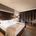 Ein modernes Hotelzimmer mit einem gemütlichen Doppelbett, einem Schreibtisch und einem Sessel vor dunklen Vorhängen.