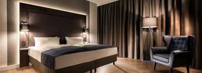 A luxurious suite features a neatly made bed, a plush armchair, and a floor lamp, perfect for a restful sleep.
