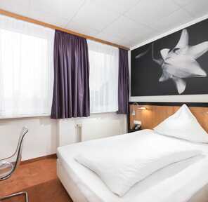 Ein modernes Einzelzimmer mit einem gemütlichen Bett, einem Schreibtisch und einem großen Blumenbild an der Wand.