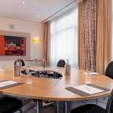 A meeting room with a round table is set for six, featuring notepads, glasses, and a vibrant wall artwork.