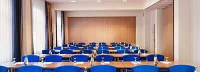 A conference room with rows of blue chairs and tables set with water bottles and notepads, ready for a meeting.
