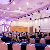 A spacious conference room with rows of chairs and tables is prepared for an upcoming event under elegant lighting.