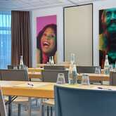 A conference room is set with chairs and tables, featuring vibrant portraits on the walls and bottled water on the tables.