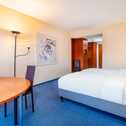 A modern hotel room features a large bed, a stylish desk, and contemporary artwork on the wall.