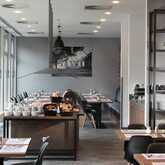 A modern breakfast room features neatly arranged tables, a buffet with pastries, and bright natural light from large windows.