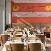 The modern restaurant interior features neatly set tables with white tablecloths and a vibrant orange wall design.