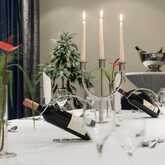 A banquet table elegantly set with candles, wine bottles, and glasses, featuring red flowers and silverware.