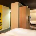 A modern family room features a bold yellow mural, cozy beds, and a stylish gray armchair by a wooden divider.