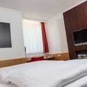 A modern hotel room features a neatly made bed, abstract artwork, and a wall-mounted TV for relaxation.