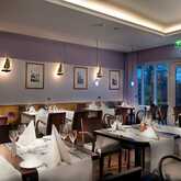 A cozy restaurant features elegantly set tables with folded napkins and warm lighting, creating an inviting dining atmosphere.