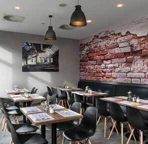 A modern breakfast room features neatly set tables and a striking brick wall accent, creating a cozy dining atmosphere.