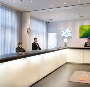 Drei Mitarbeiter stehen an einem modernen Empfangsschalter in einem Hotel, bereit Gäste zu begrüßen.