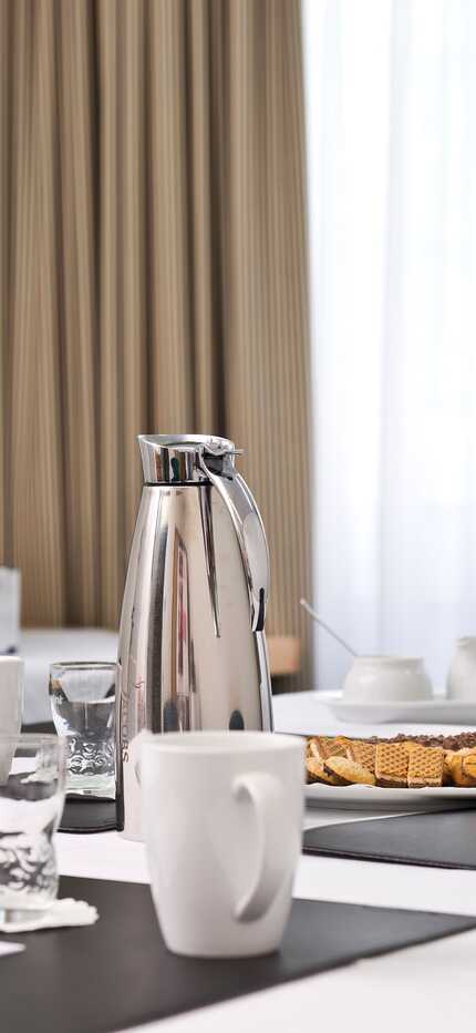Auf einem Konferenztisch im Georgengarten stehen Kaffeekannen, Tassen, Kekse und eine Vase mit orangefarbenen Blumen.