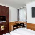 A cozy double room features a mounted TV, a wooden desk with a chair, and a modern art piece on the wall.
