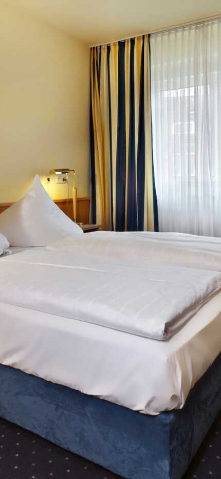 Gemütliches Doppelzimmer mit blau-gelben Vorhängen, einem großen Bett und einem Bild von Steinen an der Wand.