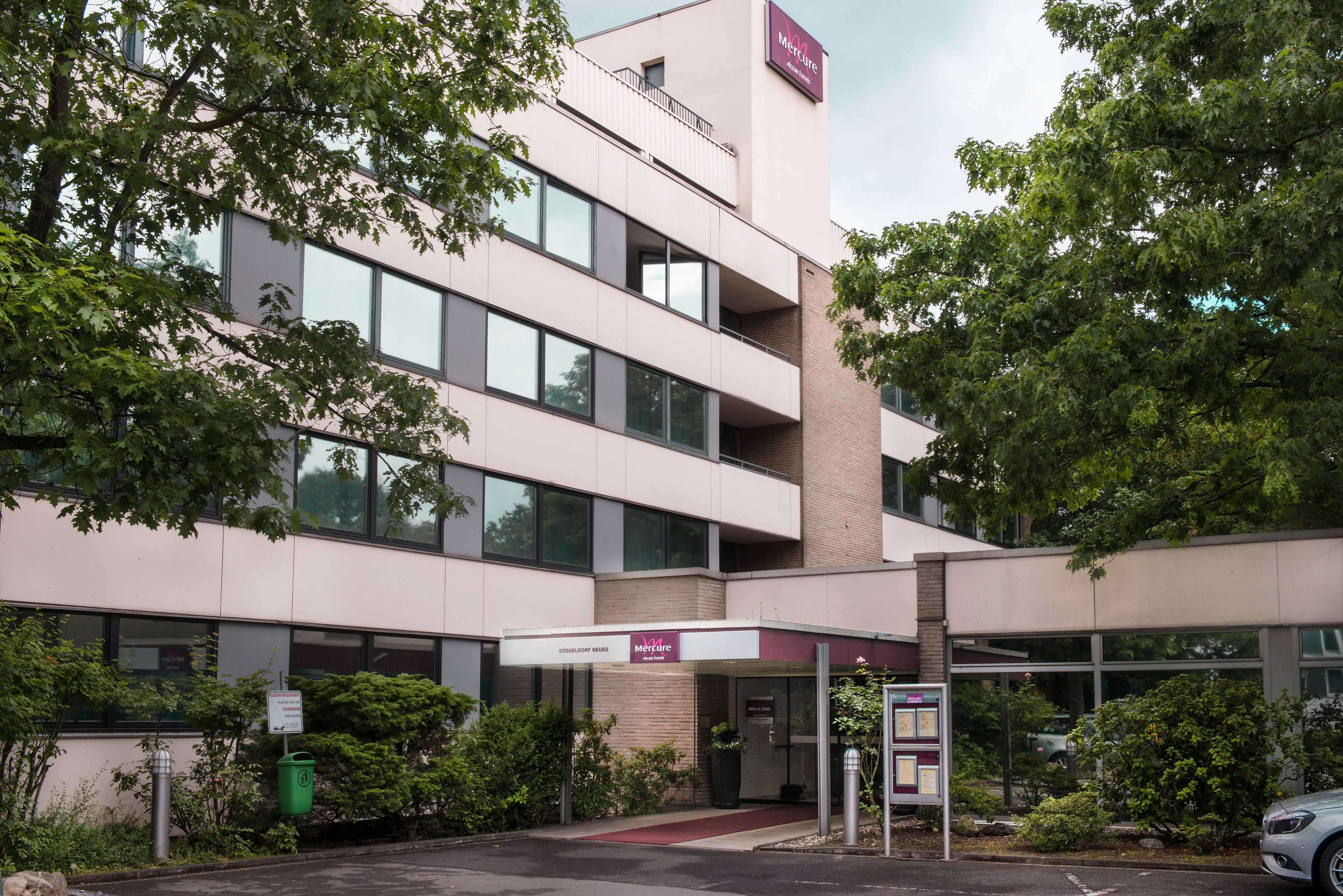 A modern hotel exterior surrounded by lush greenery, featuring large windows and a welcoming entrance.