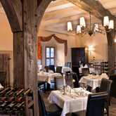 Gemütliches Restaurant mit Holzbalken, eleganten gedeckten Tischen und einem Weinregal im Vordergrund.