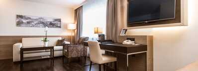 A modern business room features a sleek desk, wall-mounted TV, and comfortable seating, emphasizing a professional ambiance.