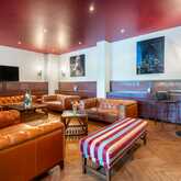 A cozy bar lounge features leather sofas, a striped bench, and art on the walls, creating a warm, inviting atmosphere.