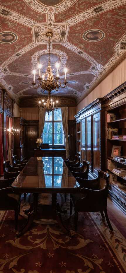 Eine elegante Bibliothek mit dekorativer Decke, hölzernen Bücherregalen und einem langen Tisch in der Mitte des Raumes.