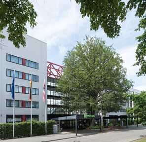 A modern hotel exterior with flags and lush trees under a clear sky creates a welcoming atmosphere.