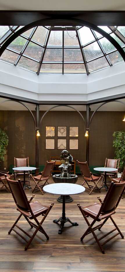 A spacious atrium lobby features a glass ceiling, elegant wooden furnishings, and lush plants, creating a welcoming ambiance.