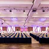 A spacious conference room is set up with rows of tables and chairs, illuminated by purple lighting for a formal event.