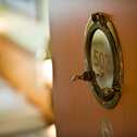 A wooden door with a round porthole labeled "502" opens to a softly lit room, highlighting nautical-themed details.