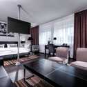 A modern suite features a cozy seating area, stylish decor, and a large bed, creating a comfortable and elegant atmosphere.
