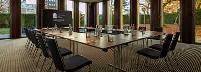 A modern meeting room setup at the Wasserturm hotel with a large table and chairs, surrounded by floor-to-ceiling windows.