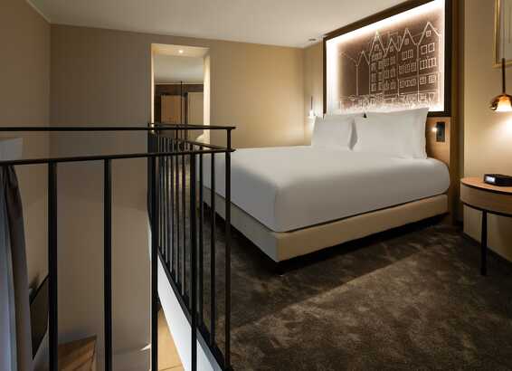 A modern bedroom features a plush bed with an illuminated cityscape headboard, adjacent to a sleek metal railing.
