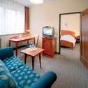 Ein gemütliches Hotelzimmer mit Sofa, Tisch und Fernseher führt in ein angrenzendes Schlafzimmer.