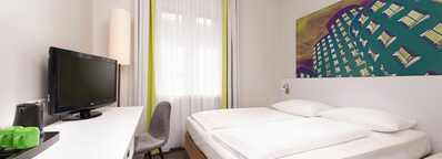 A modern hotel room features a neatly made bed, a flat-screen TV, and vibrant artwork above the headboard.