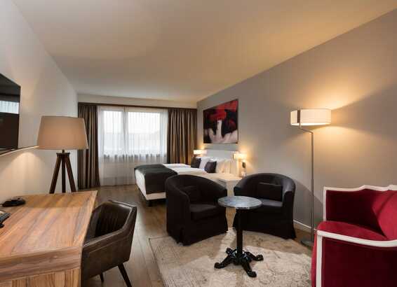A modern business room features a desk, cozy seating area, and twin beds with stylish decor and soft lighting.