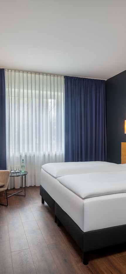 A modern hotel room features a double bed, colorful artwork, and cozy seating, creating a welcoming atmosphere.