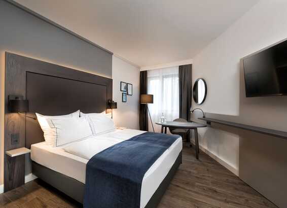 A modern business room features a queen-size bed, sleek furniture, and a wall-mounted TV for a comfortable stay.
