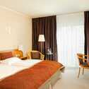 A cozy double room features a neatly made bed, desk, chairs, and a window with dark curtains.
