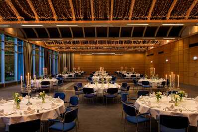 The Rhein-Lahn Saal is elegantly arranged with round tables, white linens, and illuminated by soft, decorative ceiling lights.