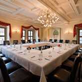 An elegant meeting room with a U-shaped table, set for a conference under a large chandelier.