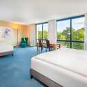 A spacious hotel room with two beds, large windows, and a view of green trees, creating a serene and inviting atmosphere.