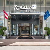 Haupteingang des Radisson Blu Hotels in Salzburg mit Flaggen und modernen Pflanzenarrangements. | © Radisson Group