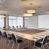 A U-shaped meeting room setup with notepads and chairs surrounds a large projection screen under modern lighting.