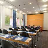 A well-lit meeting room with arranged tables and chairs, featuring notepads and water bottles under bright ceiling lights.