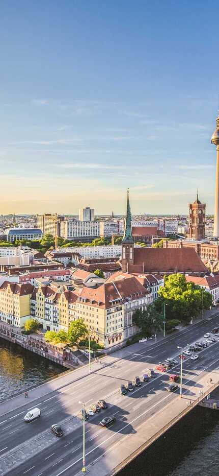 Die Berliner Skyline bei Sonnenuntergang zeigt den Fernsehturm und den Fluss, der durch die Stadt fließt.
