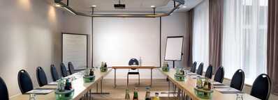 A well-lit meeting room in Hessen is set up with tables, chairs, beverages, and presentation tools for a conference.