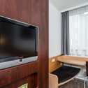 A cozy double room features a wall-mounted TV and a small wooden desk by a window with sheer curtains.